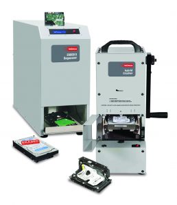 Data destruction equipment display includes an Intimus 20000G Degausser with control panel, Hybrid Crusher unit with hand crank, hard drives in various stages of sanitization, exposed circuit board, warning labels, access doors, and industrial housings on a white background