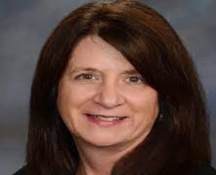 Studio head‑and‑shoulders portrait against a plain gray background, with long dark hair draped over shoulders and even, neutral lighting setup indoors
