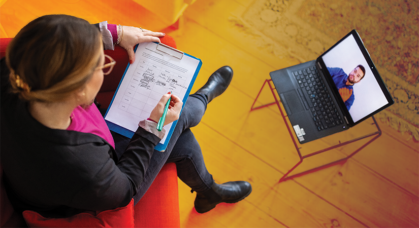 Person seated on red chair holding clipboard with notes, participating in video call on laptop atop small table; indoor setting with neutral tones