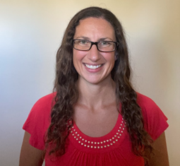 Person wearing a bright red short-sleeve top with a round neckline decorated with small white beads, standing against a plain beige wall indoors