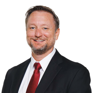 Individual in black suit, white shirt, and red tie stands against plain white background; professional attire.