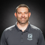 Person wearing a dark gray Portland Police polo shirt with embroidered badge and “Sergeant” text, standing against a black studio background with soft lighting.