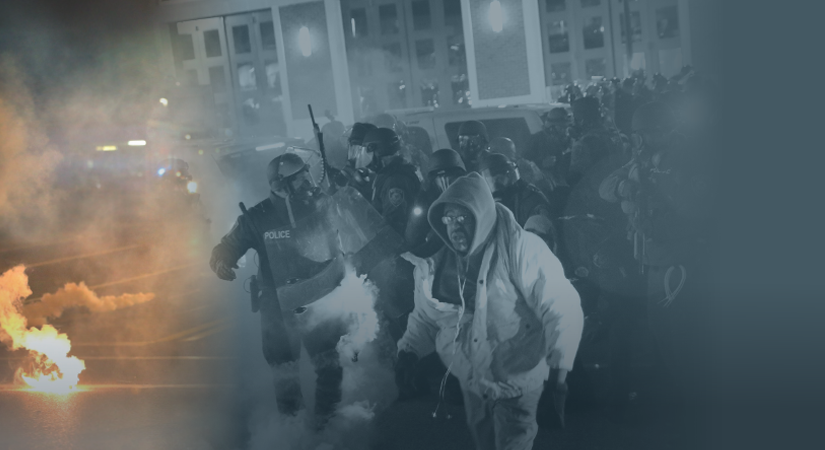 Officers in riot gear advance through tear gas; one holds baton, another shield; hooded civilian moves away amid smoky, tense urban backdrop.