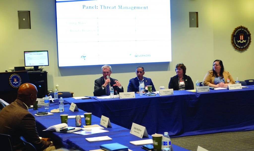 Four-person panel on Threat Management sits before screen with topic and names; attendees at round tables with nameplates, docs, drinks; FBI emblem