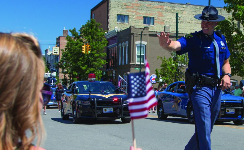 State Trooper waves at bystander as he walks in the Traverse City National Cherry Festival Parade