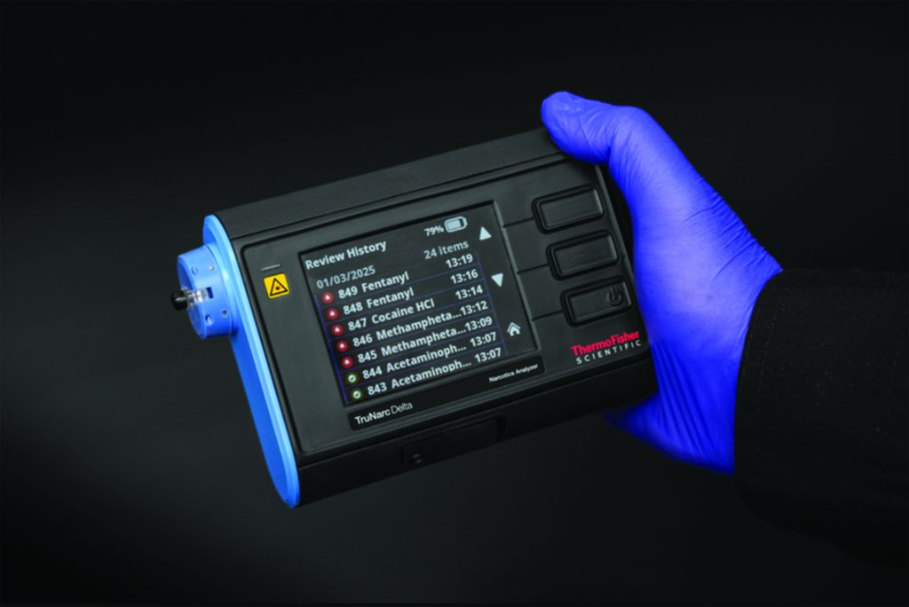 Gloved hand holds TruNarc Delta device showing review history of detected substances: Fentanyl, Cocaine HCL, Meth, and Acetaminophen on screen