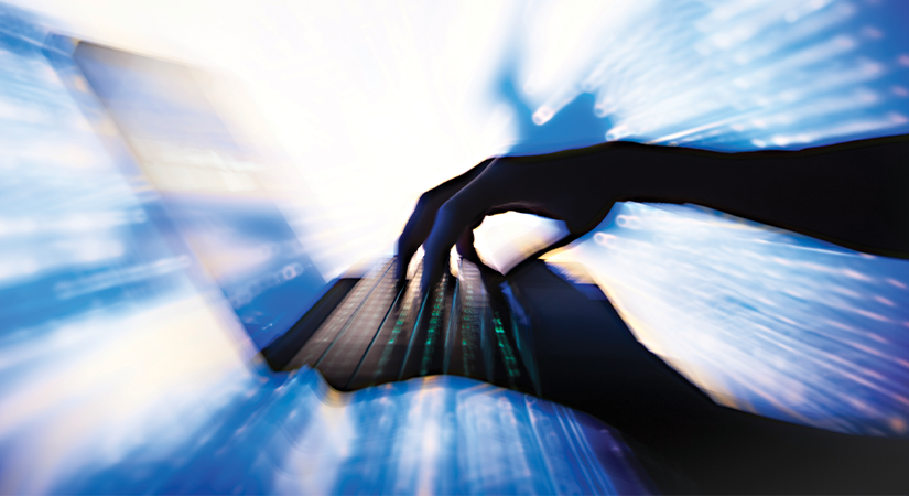 A silhouetted hand types on a laptop keyboard as bright blue and white digital streaks radiate outward, creating a dynamic motion effect around the device