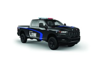 Black RAM heavy‑duty police pickup shows blue accent stripe, ‘LAW’ markings, emergency light bar, grille lights, crew cab, and rugged wheels on white background
