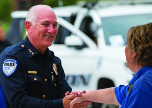 A police officers from Richardson Police Department standing together in front of their car. They are dressed in formal uniforms, showcasing leadership and camaraderie within the department shaking hands with a civilian
