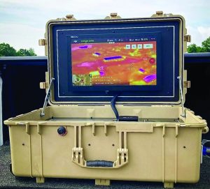 Rugged tan field case with a built‑in LCD showing a drone’s thermal imaging feed, open on support struts with cables and controls visible against an outdoor backdrop