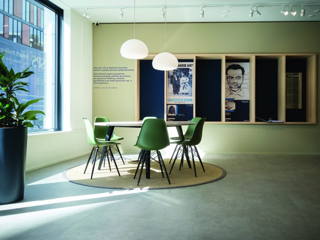 A police officer from Utrecht, dressed in tactical gear, standing in front of a modern building. The officer is actively engaged in a public safety operation, demonstrating the preparedness and professionalism of the police force.