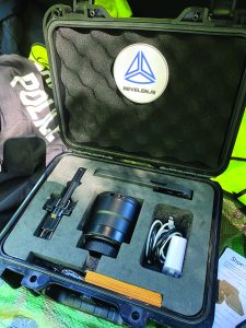 Open hard case showing Revelen.AI‑branded lid and foam‑fitted tools, including a scanner probe, large lens, cables, and accessories beside police gear