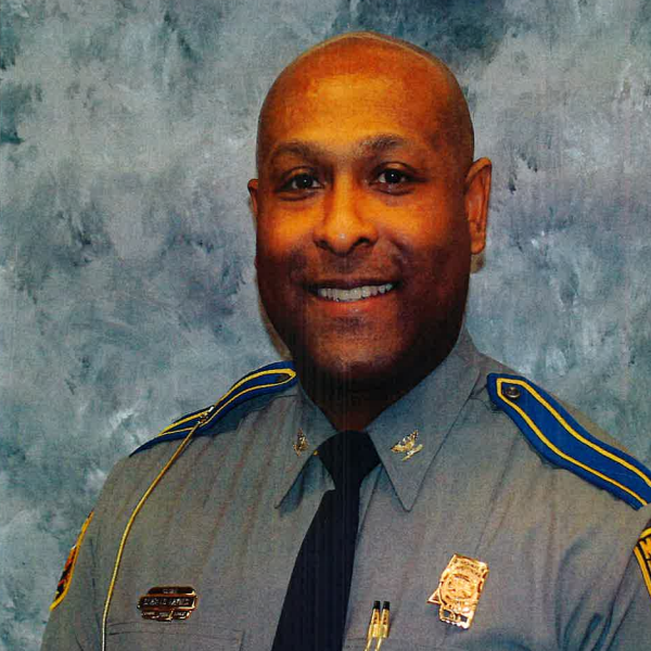 Mississippi Highway Patrol officer shown from shoulders up in uniform with badge, nameplate, and shoulder patches; mottled gray background