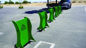 Row of green Delta Scientific portable vehicle barriers connected by cables in an asphalt parking lot with a parked SUV and desert landscape in background