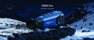 Blue TS004 Pro thermal monocular resting on a snow‑covered rock in a mountain landscape, with product text above and icy details on the device housing
