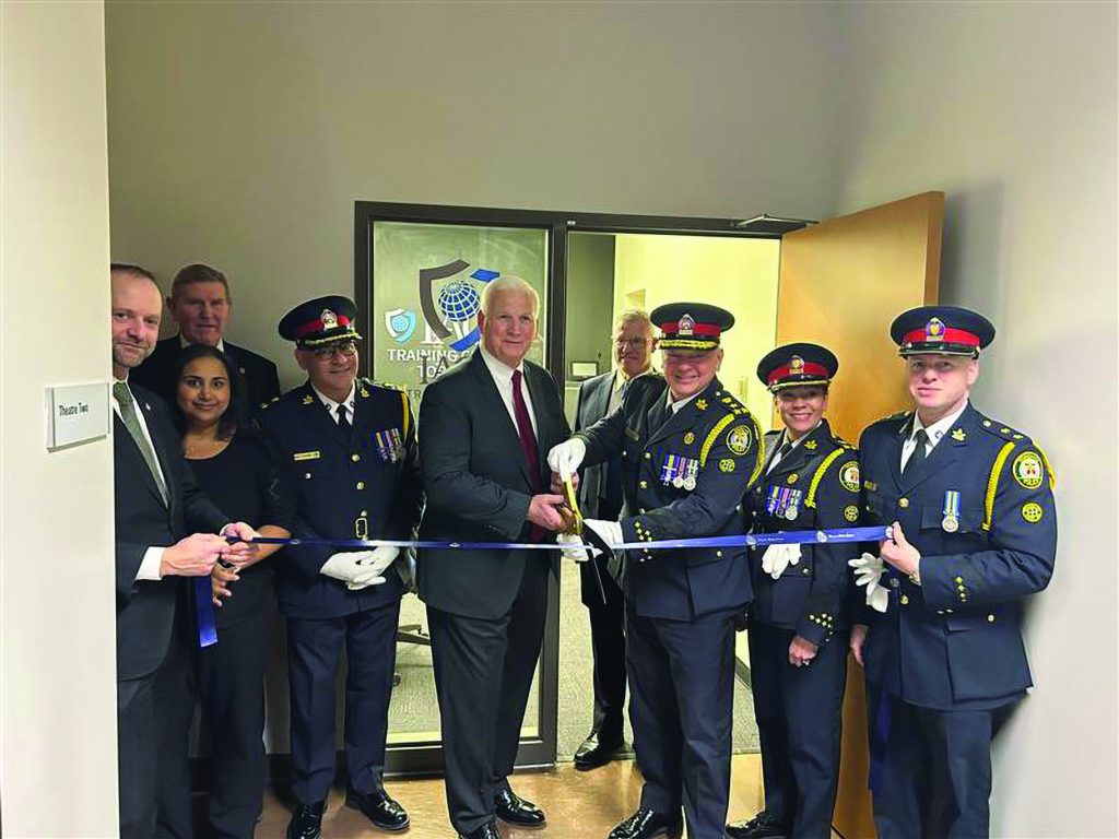 Law enforcement officials and suited man cut blue ribbon at entrance of training center; door sign reads 'Training Center 1945'