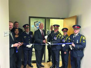 Law enforcement officials and suited man cut blue ribbon at entrance of training center; door sign reads 'Training Center 1945'