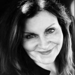 Black and white photo of a person with long, wavy hair, highlighting hair texture and shoulders against a dark, shadowed background