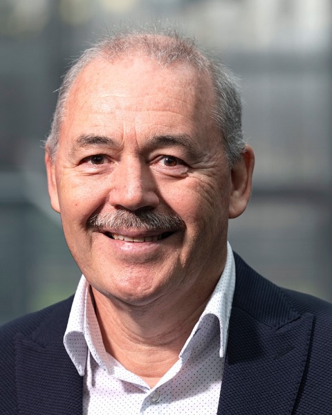 Person wearing a dark blazer over a white dress shirt with subtle dotted pattern, standing indoors against a softly blurred background with natural light