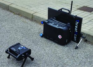 Portable ThreatScan X-ray panel, hard case, and tripod-mounted scanner set on roadside pavement near curb during field inspection setup