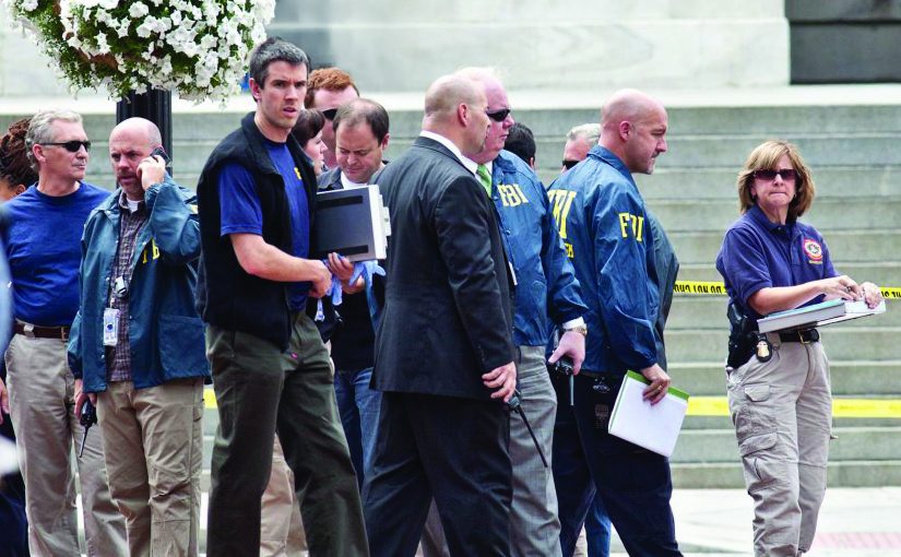 A group of investigators and uniformed personnel stand near concrete steps marked with yellow tape, holding documents and equipment beside a hanging planter.