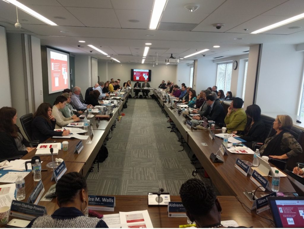 Large conference room with U-shaped table setup, filled with law enforcement professionals; presentation slides shown on screens at both ends